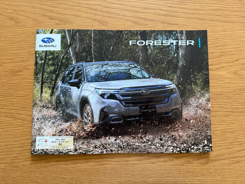 木の机に置いたスバル フォレスターのカタログ。表紙には森の中を走るフォレスターが写っている。
